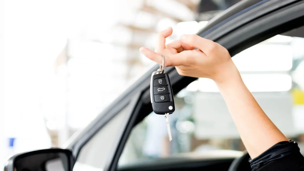 A woman holding car keys outside her car window.