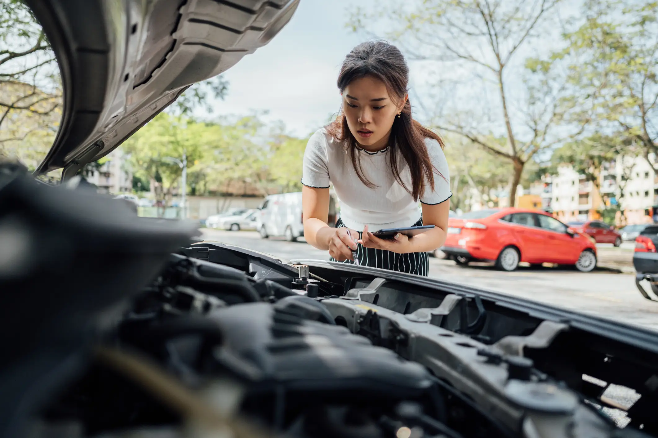 A concerned woman looking at her car engine.
