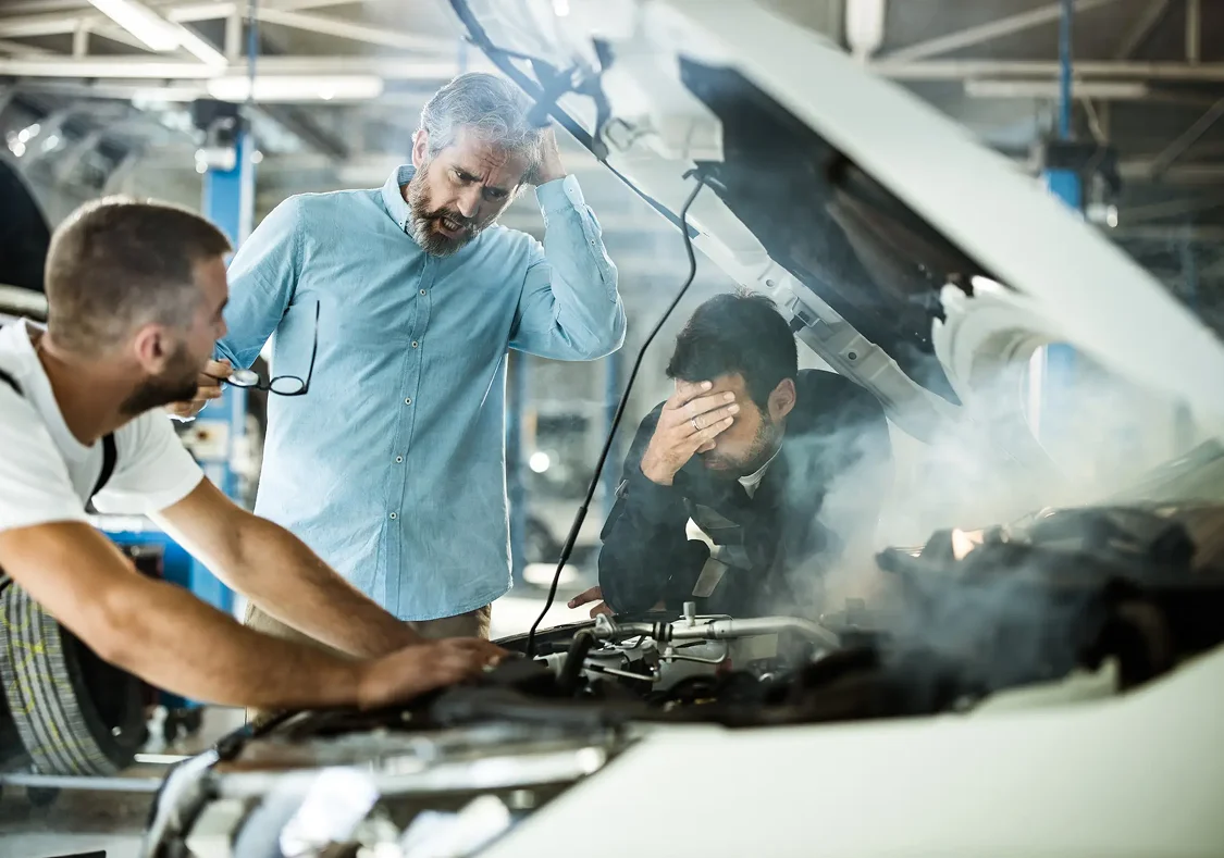 A car smoking when a mechanic is looking at it and the owner is stressed.