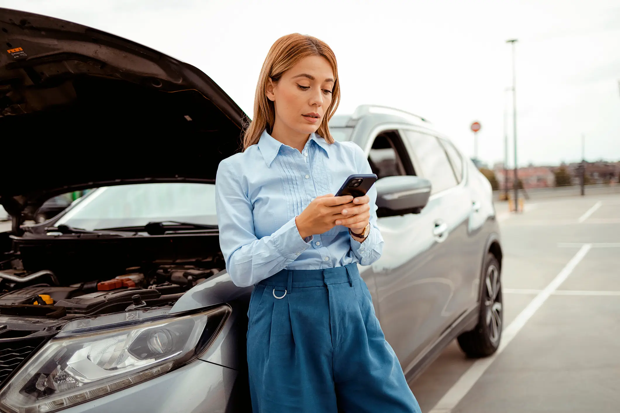 A woman looking on her phone if her car is a lemon.