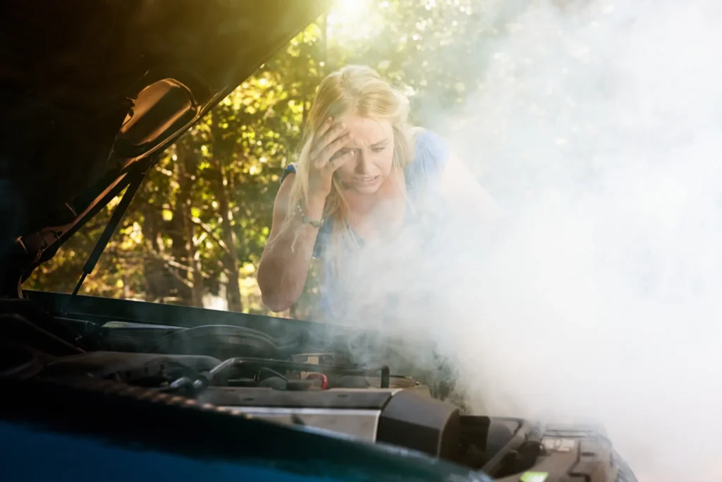 A woman looking at a car engine that is smoking like crazy.