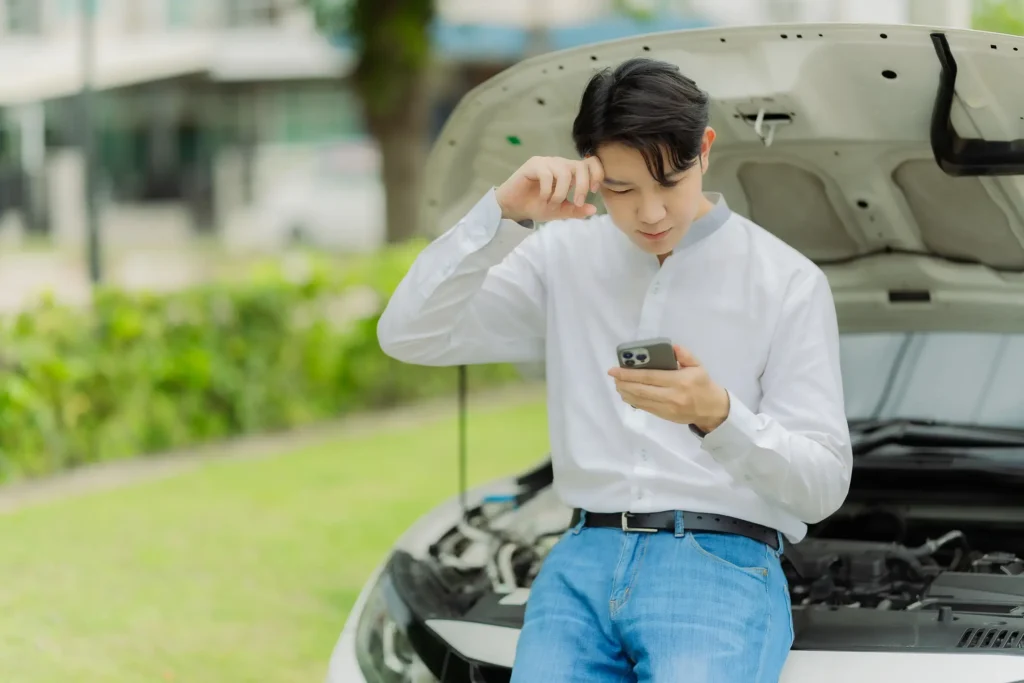 A man looking at his phone to find a solution for his defective car.