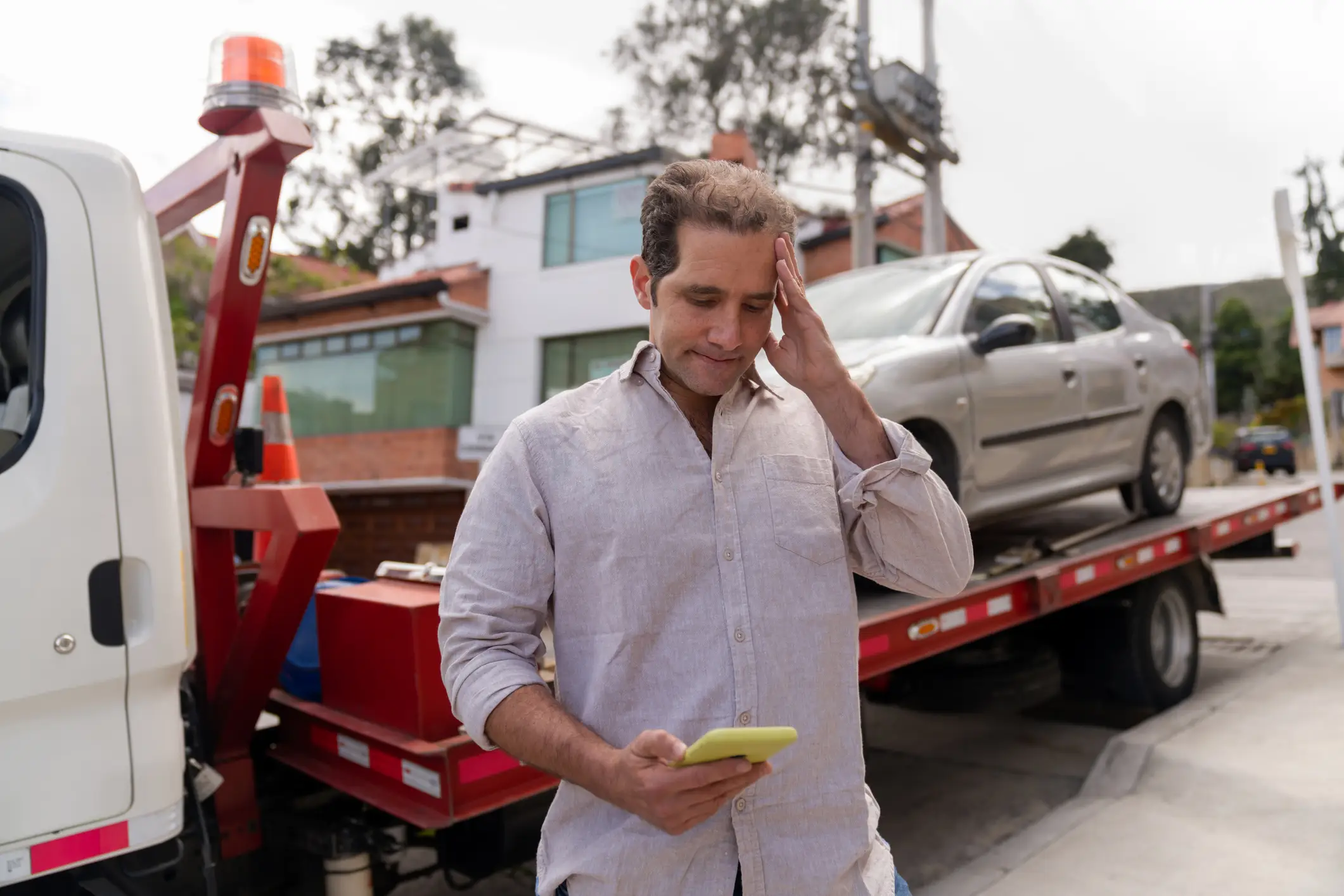A stressed man looking at his phone when his car is broken down.