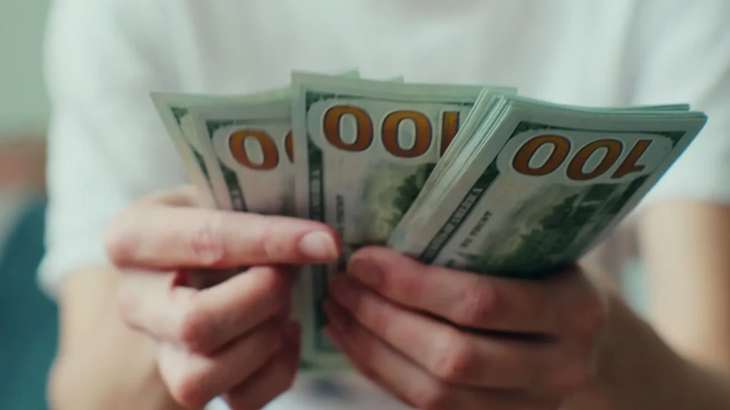 A person holding a stack of hundred dollar bills.